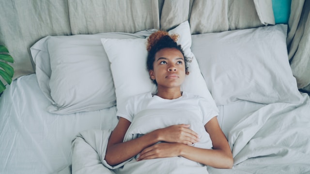 Person lying in bed resting their head on white pillows.