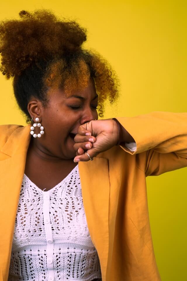 Woman in a yellow blazer yawning with her eyes closed.